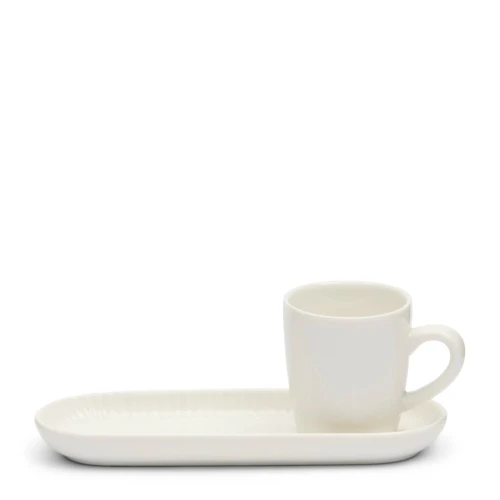 Kubek ceramiczny w kolorze białym, stojący na prostokątnym podstawku o minimalistycznym designie. Ujęcie z boku ukazuje subtelne wykończenie podstawka oraz delikatny kształt kubka z małym uchwytem. Tło proste, jednolite.