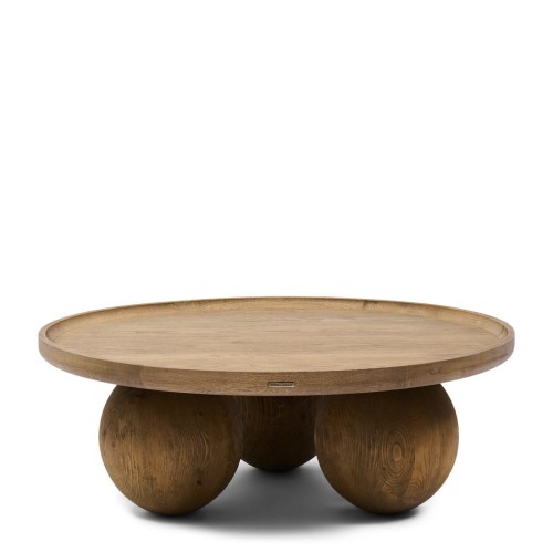 Designerski stolik kawowy Rockefeller Riviera Maison w kolorze naturalnego drewna, okrągły, z płaskim blatem i podpórkami w formie dużych kul. Stolik widoczny z boku, umieszczony na białym tle. Wyróżniający się minimalistycznym wyglądem.