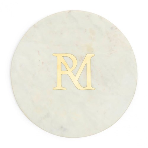 Biała, okrągła marmurowa podstawa RM Marble Riviera Maison z delikatnymi żyłkami i złotym logo „RM” na środku, na płaskiej powierzchni, podkreślająca elegancję naturalnej faktury marmuru.