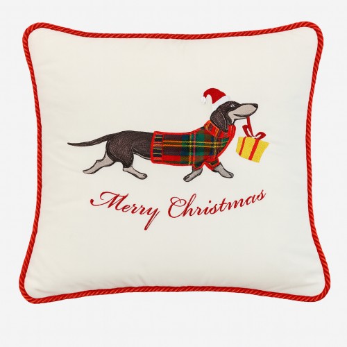 Poduszka dekoracyjna z haftem przedstawiającym psa w czerwonej czapce świątecznej i sweterku w kratę, trzymającego prezent. Na białym tle widoczny napis Merry Christmas. Poduszka ma czerwone wykończenie.