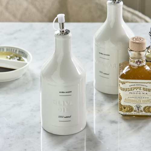 Pojemnik na ocet Capri Riviera Maison w białym ceramicznym wykończeniu, z metalowym dozownikiem. Etykieta z napisem VINEGAR w ciemnym kolorze. Stoi na marmurowym blacie obok pojemnika na oliwę i butelki z oliwą.