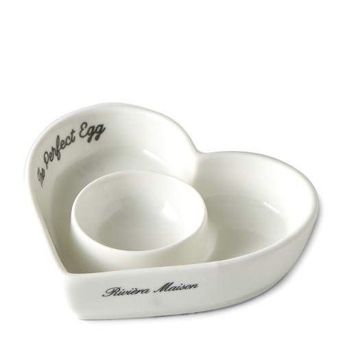 Stojak na jajko w kształcie serca wykonany z białej ceramiki, z napisem The Perfect Egg oraz logo Riviera Maison. Produkt w pozycji leżącej, z dwoma wgłębieniami na jajka, o miękkich krawędziach i gładkiej fakturze.