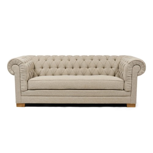 Sofa Crescent Dune Sand Riviera Maison w kolorze piaskowym, z pikowanym oparciem i zaokrąglonymi bokami. Ustawiona w pozycji leżącej, na drewnianych nóżkach, z prostym, minimalistycznym tłem. Wykonana z materiału tekstylnego.