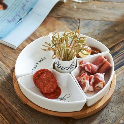 Zestaw Tapas Party Plate Riviera Maison składa się z okrągłej białej miski podzielonej na cztery sekcje, z drewnianą podstawą. Widzimy w niej plastry salami, wędliny i wykałaczki w pojemniku z napisem Pinchos. Idealny do serwowania tapas.