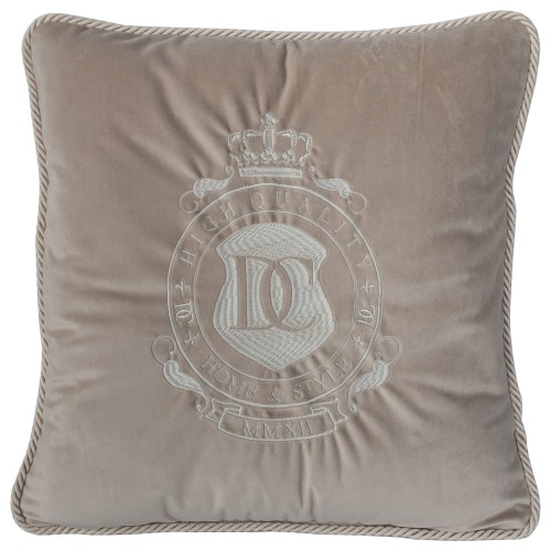 Poduszka haftowana dekoracyjna w kolorze beżowym z miękkiego welwetu. Widoczny centralny haft z logo DC oraz napisem HIGH QUALITY HOME & STYLE. Ujęcie frontalne. Krawędź poduszki wykończona plecionką, rozłożona na płaskiej powierzchni.