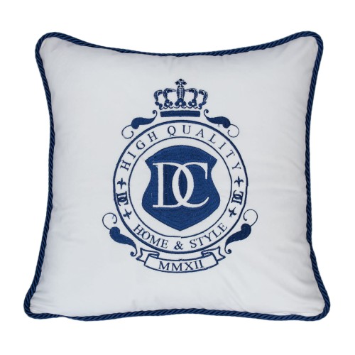 Poduszka dekoracyjna haftowana w kształcie kwadratu, z białym tłem i granatowym haftem. Widoczny nadruk z logo DC oraz hasłem HIGH QUALITY HOME & STYLE. Wzdłuż krawędzi ozdobny granatowy szew. Produkt ułożony płasko.