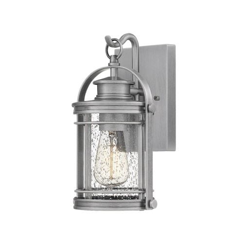 Kinkiet zewnętrzny Benev S wykonany z aluminium w kolorze srebrnym, o wymiarach 16x16x29 cm. Produkt montowany na ścianie, z widoczną szklaną osłoną z efektem kropel. Oświetlenie o klasycznym kształcie, z metalowymi detalami.