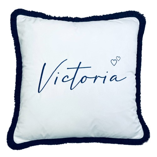 Poduszka kwadratowa z białym, jedwabistym pokryciem oraz granatowym, frędzlowym wykończeniem. Widoczny haft imienia Victoria w eleganckim kroju pisma. Produkt leży płasko na neutralnym tle, ukazując detale wzoru i teksturę materiału.