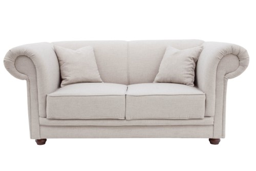 Dwuosobowa sofa Chesterfield w jasnoszarym kolorze, z wysokimi bokami i okrągłymi podłokietnikami. Wyposażona w dwa dodatkowe poduszki. Produkt widoczny z przodu, na białym tle, w rozłożonej pozycji. Wymiary 180x105x80 cm, tapicerka materiałowa.
