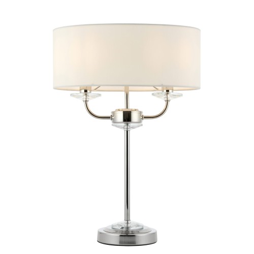 Lampa stołowa Nixon o wysokości 54 cm, z metalowym stelażem w kolorze niklu oraz okrągłym kloszem z białej tkaniny. Stoi na okrągłej, błyszczącej podstawie, z dwiema przezroczystymi dekoracjami przy mocowaniach.