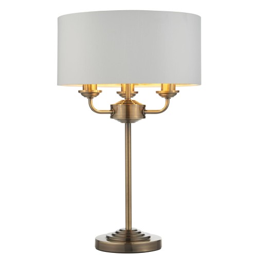 Lampa stołowa Highclere w kolorze mosiądzu, z białym, papyrusowym abażurem. Stojąca konstrukcja z trzema źródłami światła, z widocznymi detalami mocowania. Ujęcie frontalne na jednolitym tle. Wysokość 50 cm.