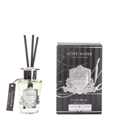 Dyfuzor Cote Noire Private Club w cylindrycznym, przezroczystym szklanym flakonie z metalowym, błyszczącym kominem i pięcioma czarnymi patyczkami, w eleganckim czarno-białym opakowaniu z logo.