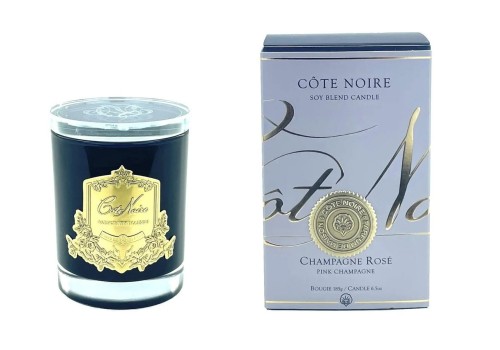 Sojowa świeca Cote Pink Champagne Gold w czarnym słoju z przezroczystą pokrywką i złotą etykietą. Obok opakowanie z jasnoniebieskim nadrukiem i napisami Côte Noire oraz Champagne Rosé.