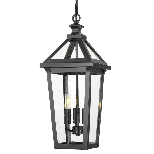 Lampa zewnętrzna wisząca, wysokość 58 cm, w czarnej metalowej oprawie z przezroczystym szkłem. Zawiera trzy źródła światła. Kąt ujęcia frontalny, wisząca, z wyeksponowanymi detalami konstrukcji. Białe tło podkreśla elegancję produktu.