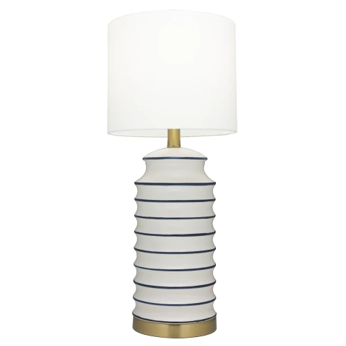 Designerska lampa stołowa w stylu coastal o wysokości 61 cm, z okrągłym, białym kloszem i podstawką w złotym kolorze. Korpus w kształcie cylindrycznym, z wyraźnymi, poziomymi zdobieniami w granatowym kolorze, stoi na stabilnej podstawie.