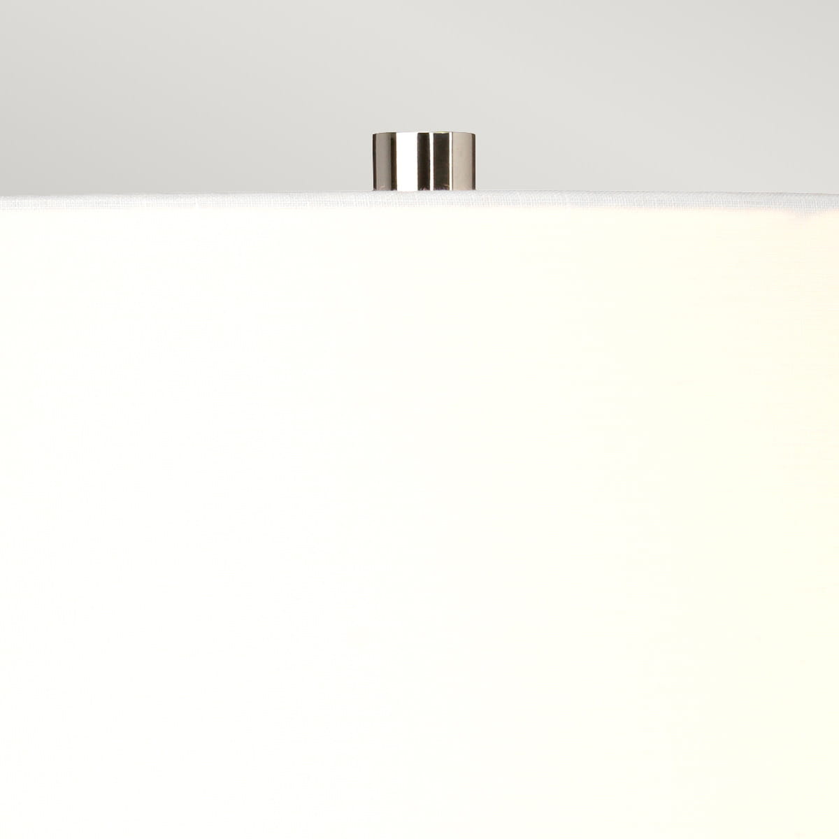 Lampa stołowa Mussa z białym, tekstylnym kloszem, metalowym uchwytem w kolorze chromu. Ujęcie z góry, pokazujące szczegóły mocowania i kształt klosza. Tło jasne, neutralne, co podkreśla minimalistyczny design produktu.