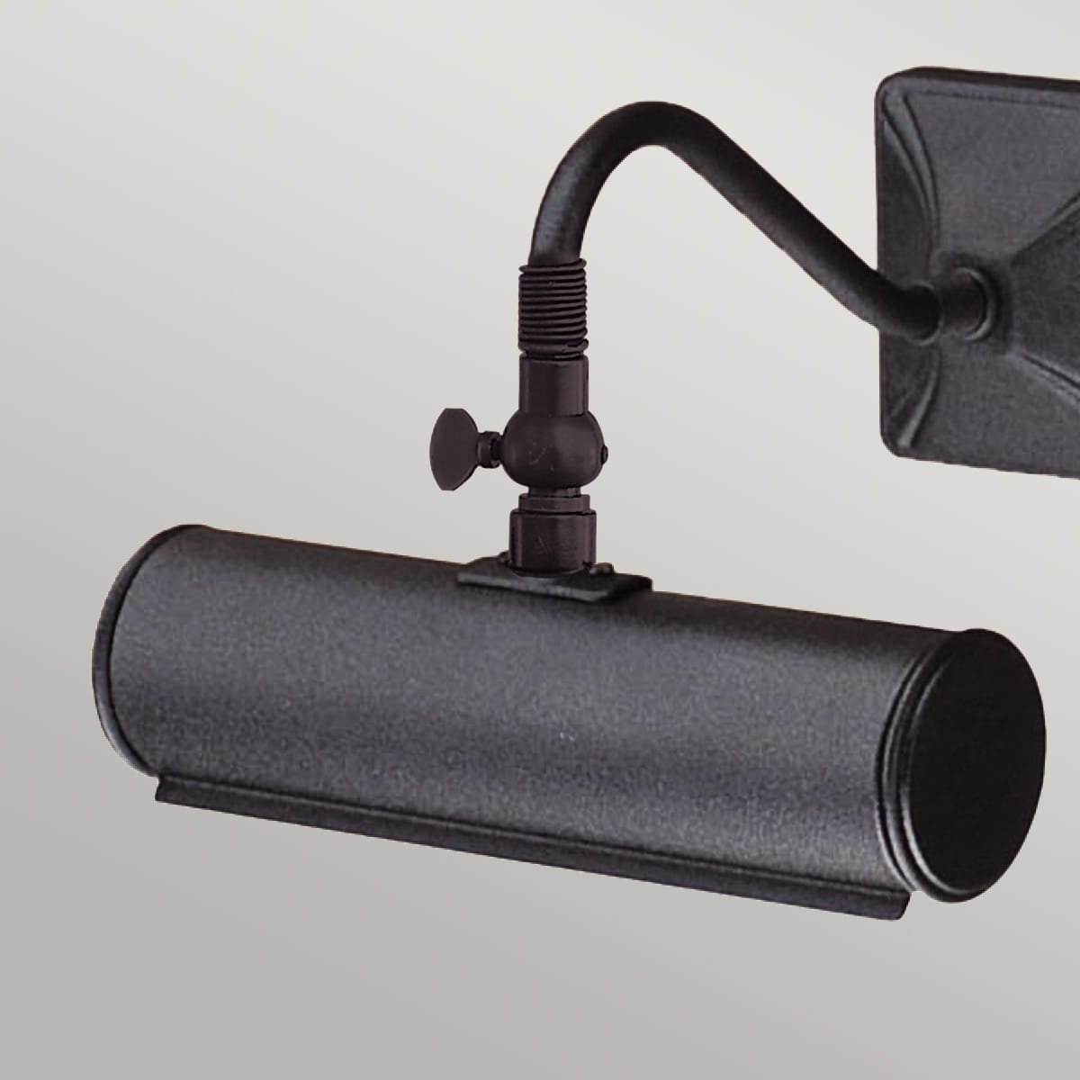 Mały kinkiet galeryjny Cortona w kolorze czarnym, wykonany z materiału metalowego. Produkt wisi na ścianie, z zauważalnym regulowanym mocowaniem. Okrągły cylinder lampy ma matową powierzchnię, co podkreśla minimalistyczny design.
