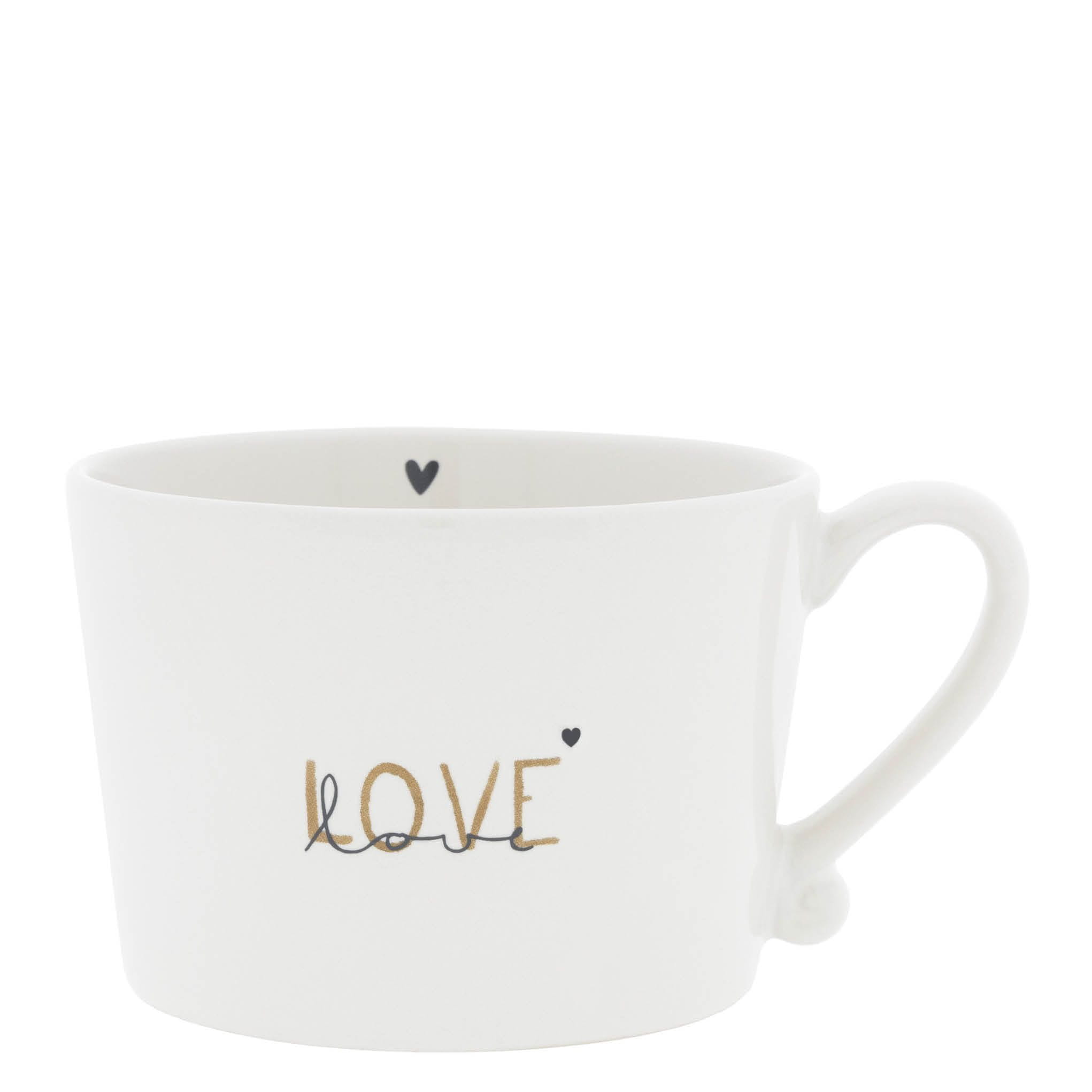 Kubek ceramiczny w kolorze białym z napisem „love” w złotym i czarnym kolorze, o zaokrąglonym kształcie i uchwycie. Widok frontalny, produkt stoi na równym podłożu. Wewnątrz widoczny mały czarny serce.