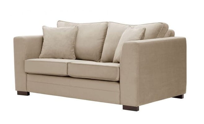 Sofa dwuosobowa w kolorze jasnobeżowym z niskimi, prostokątnymi podłokietnikami, z dwoma poduszkami oparciowymi. Produkt stoi na ciemnych, prostokątnych nóżkach. Ułożenie jest frontalne, bez widocznych detali wzorów.