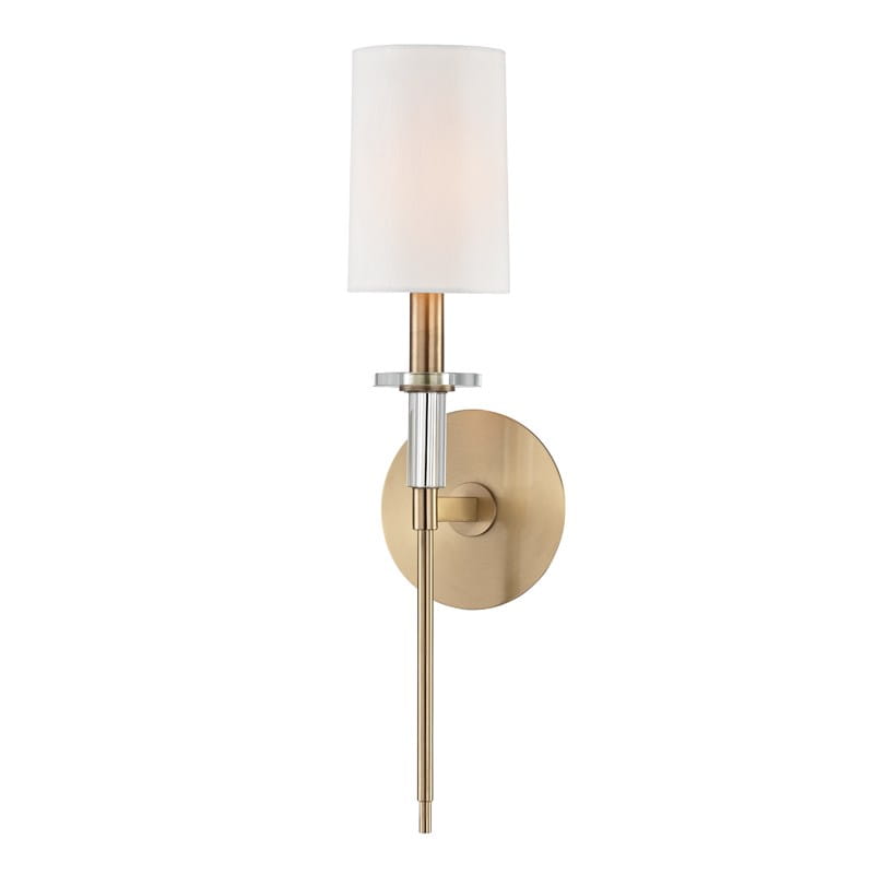 Stylowy kinkiet Amherst w kolorze mosiądzu z białym, cylindrycznym kloszem. Ujęcie frontalne, produkt zamontowany na ścianie. Widoczny ozdobny trzon z metalowymi detalami, minimalistyczny design. Białe tło podkreśla elegancję kinkietu.