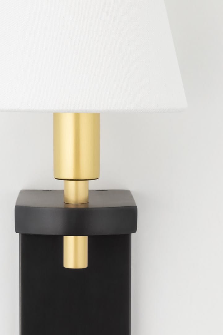 Klasyczny kinkiet Dooley w kolorze mosiądzu i czerni. Lampa ma biały, tekstylny klosz i prostą, geometryczną formę. Ujęcie frontalne, produkt zamontowany, z widocznym eleganckim wykończeniem. Tło białe, co podkreśla detale kinkietu.