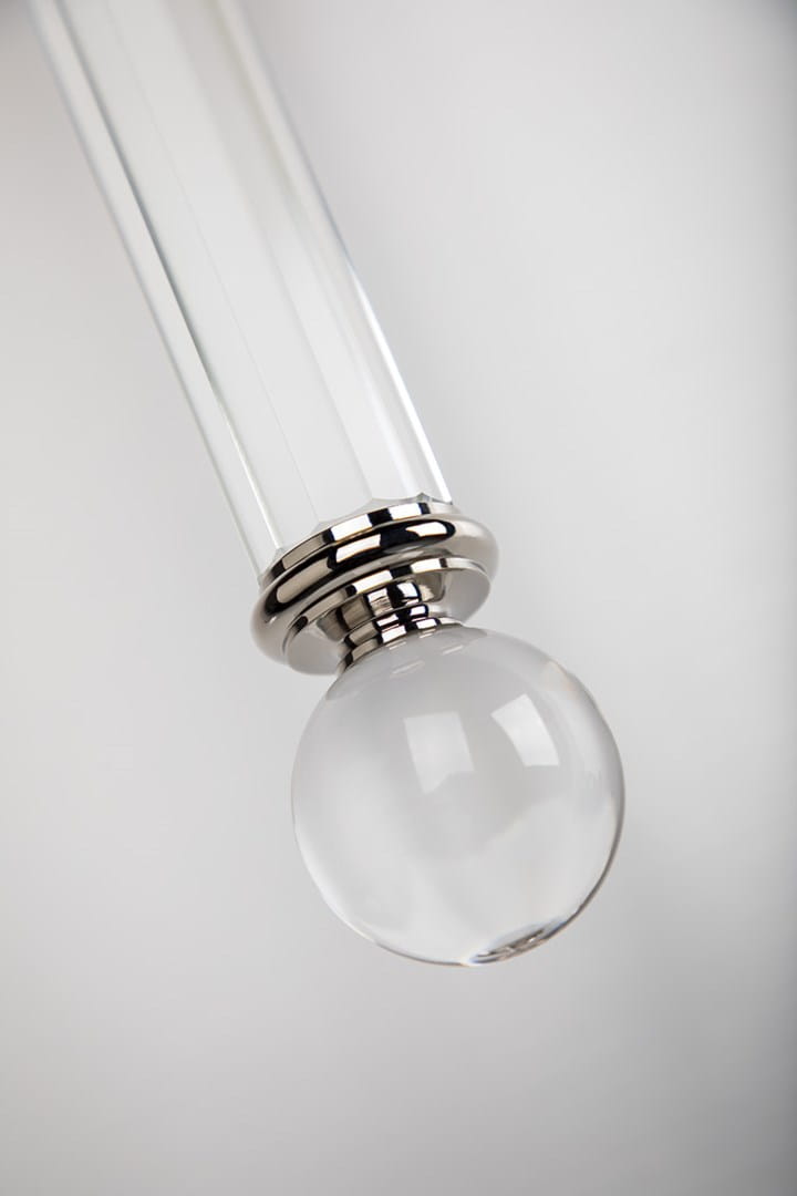 Elegancki kinkiet Gordon w kolorze mosiądzu, z przezroczystą szklaną kulą. Produkt widoczny w zbliżeniu, ukazujący detale mocowania oraz lśniący metalowy element u góry. Tło neutralne, co podkreśla elegancję kinkietu.