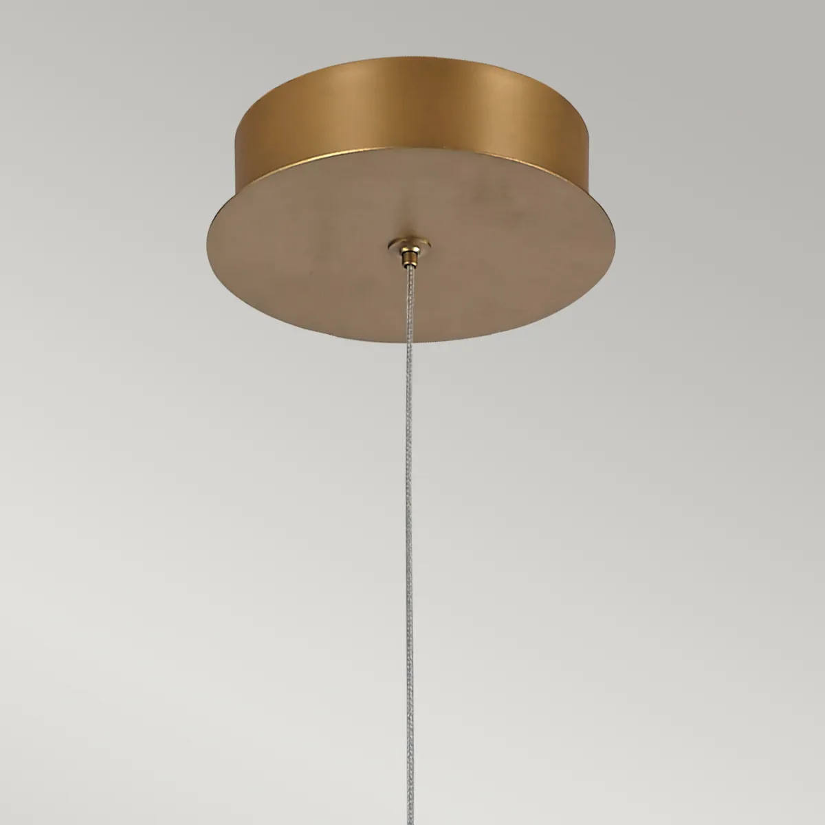 Sufitowa lampa wisząca w kolorze szczotkowanego złota z okrągłym mocowaniem i metalowym przewodem. Produkt widoczny z góry, eksponujący kształt sufitu lampy i surowy materiał, wpisujący się w nowoczesne aranżacje wnętrz.