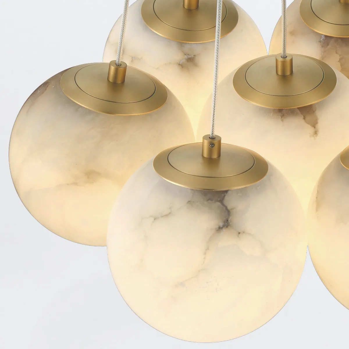 Wisząca lampa designerska, kulista, z transparentnego materiału z delikatnym, marmurkowym wzorem. U góry złoty element mocujący z przewodem. Produkt w zestawie z kilkoma lampami, zawieszony, w świetle, na jasnym tle.