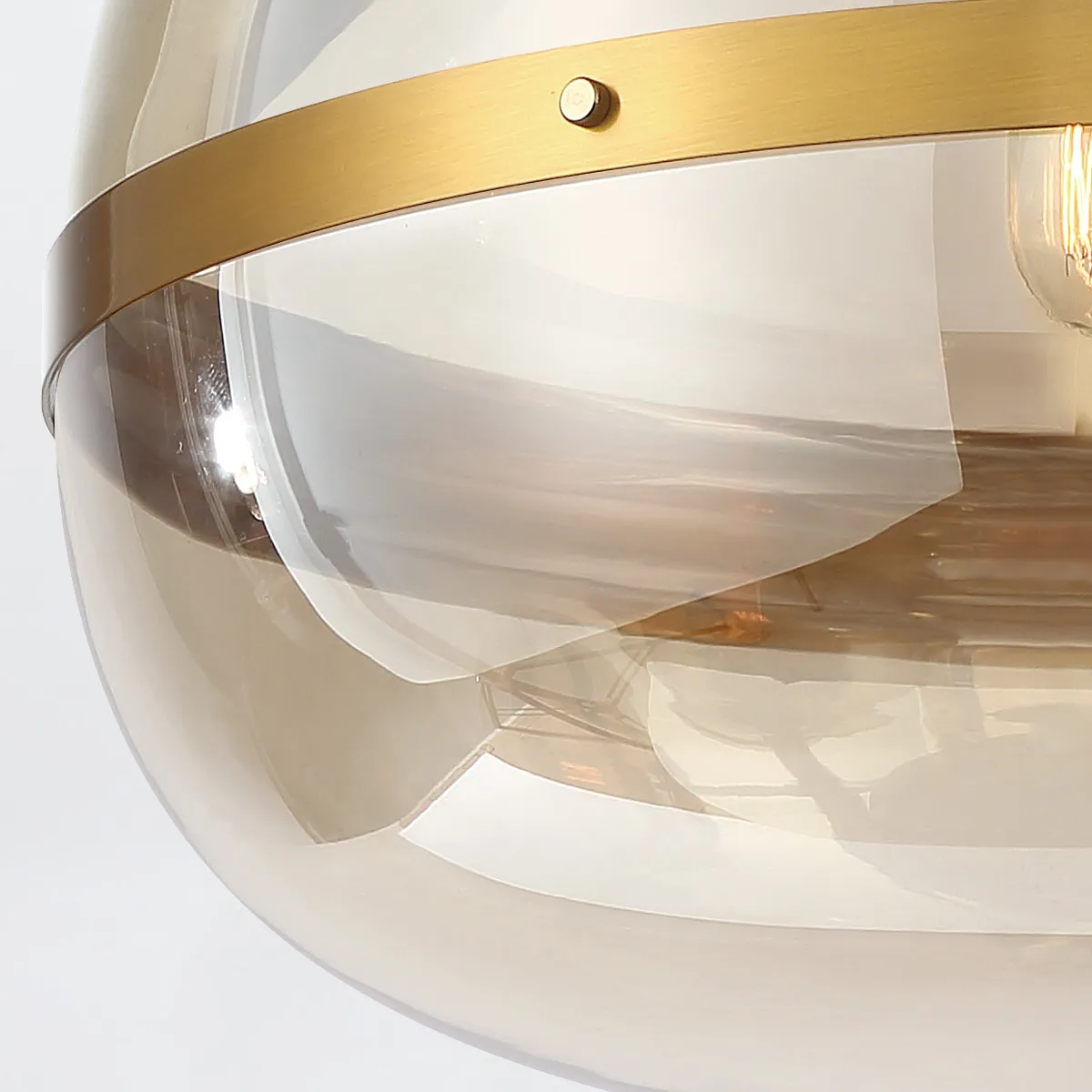 Designerska lampa wisząca Nottingham w kolorze mosiężnym, z przezroczystym kloszem. Widok w zbliżeniu na detal montażu oraz metalową obręcz. Klosz ma okrągły kształt i gładką fakturę. Produkt zamontowany, w świetle naturalnym.