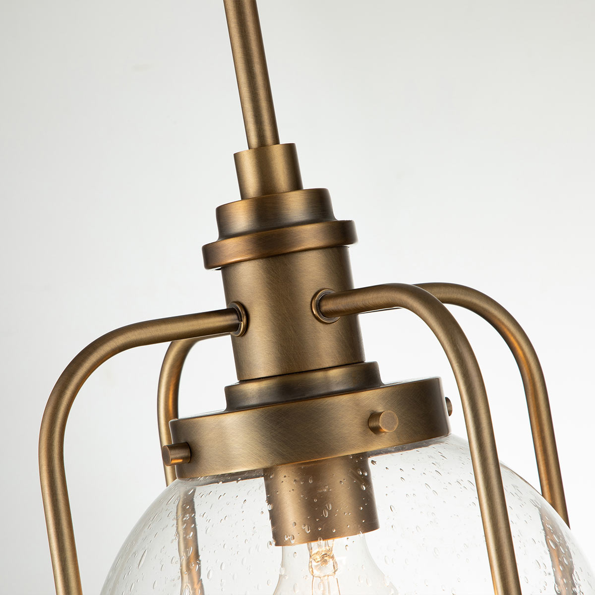 Lampa wisząca Triocent w mosiężnym wykończeniu, z przezroczystym kloszem o kształcie kulistym. Ujęcie z góry pokazuje detale mocowania oraz metalowe ramiona podtrzymujące klosz. Tło jasne, minimalistyczne, podkreślające elegancję produktu.