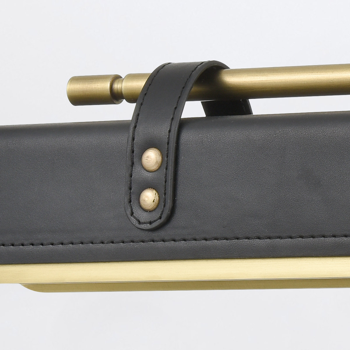 Kinkiet Led Valise Vintage z brązowym uchwytem ze skóry smokingowej, z metalowymi elementami w kolorze mosiądzu. Ujęcie z bliska, pokazujące szczegóły przymocowania uchwytu do lampy. Tło białe, co podkreśla kolory i fakturę materiałów.