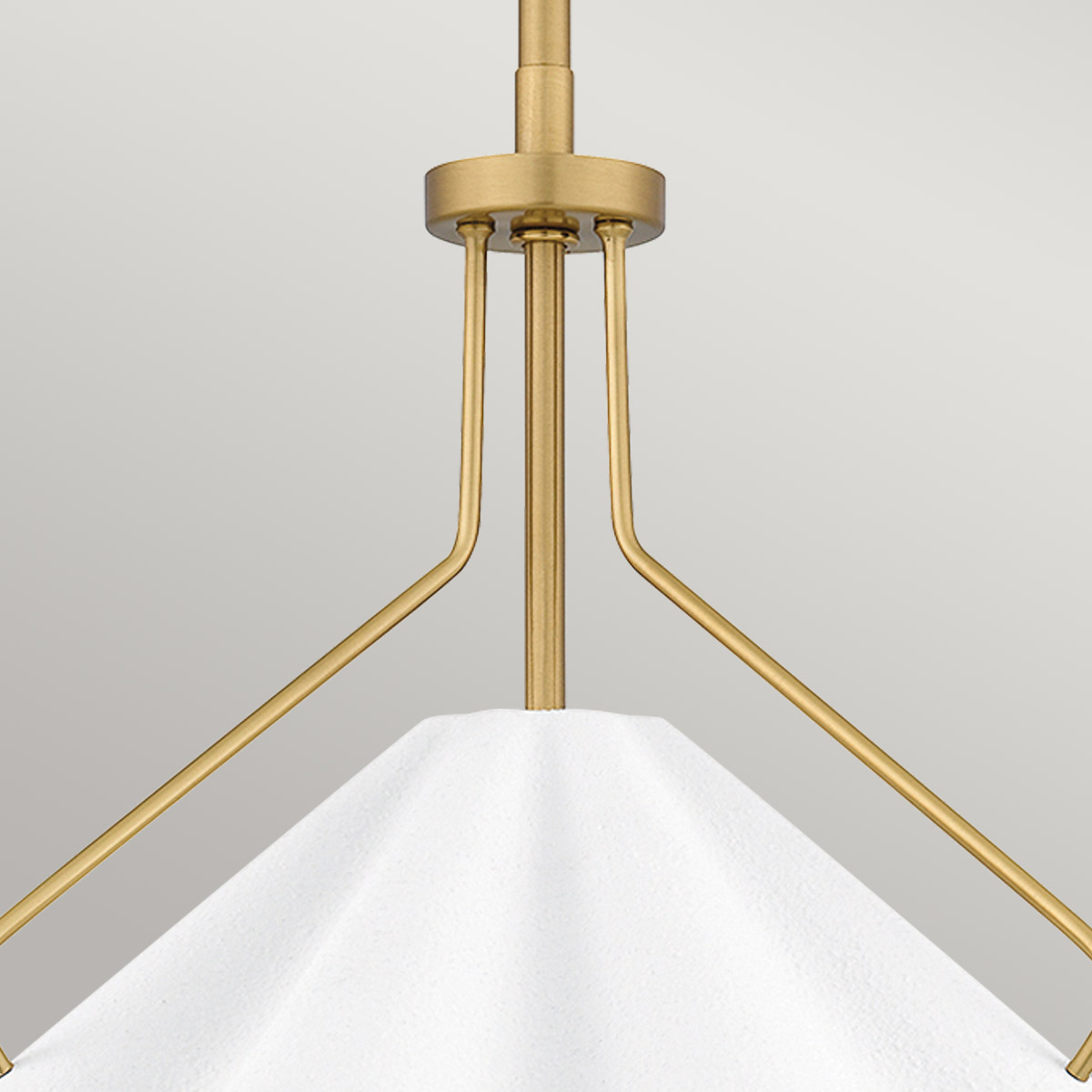 Lampa wisząca Mejia z postarzanym mosiądzu, o stożkowym kloszu w białym kolorze. Fragment produktu ukazany z góry, prezentujący detale uchwytu oraz konstrukcji. Tło jednolite, szare, które podkreśla elegancki charakter lampy.