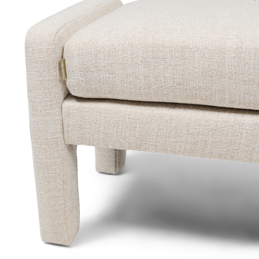 Puf ławka Avalon w kolorze antique white od Riviera Maison. Prosta, kwadratowa forma z miękkim siedziskiem pokrytym teksturowanym materiałem. Widoczne boczne wykończenie oraz złote logo marki. Produkt stoi na niskich nóżkach.
