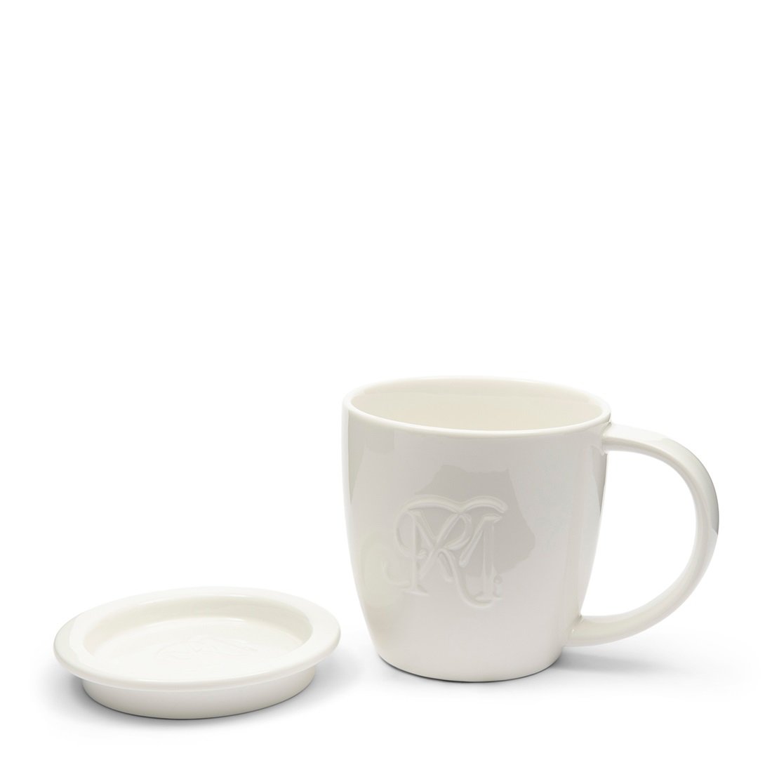 Biały kubek ceramiczny z uchwytem, o gładkiej powierzchni i zaokrąglonym kształcie, z wytłoczonym logo RM. Obok znajduje się talerzyk, również w białym kolorze, przeznaczony na torebki herbaty. Produkt ustawiony frontalnie na jasnym tle.