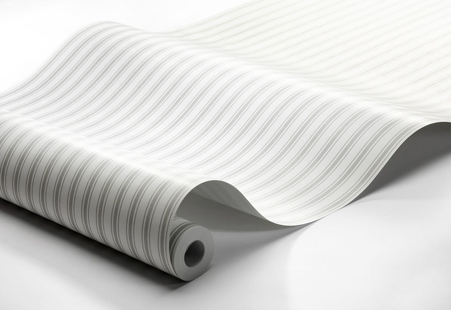 Tapeta Marstrand II Aspo Stripe w kolorze szarym i białym, z falistym wzorem w poziome paski. Produkt leży na białym tle, prezentując szeroką rolkę tapety w częściowo rozwiniętej formie.