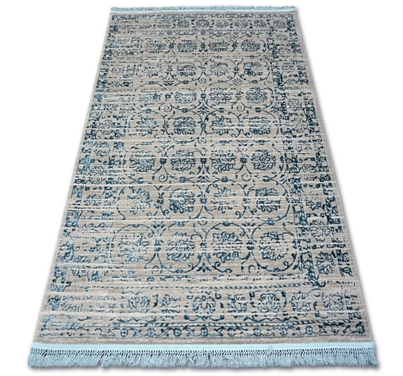 Dywan Tebanny w kolorze szaro-niebieskim o wymiarach 160x230 cm, z delikatnym wzorem roślinnym. Produkt leży na płasko, z frędzlami na krótszych krawędziach, na jasnym tle. Tekstura jest gładka, co podkreśla elegancki wygląd.