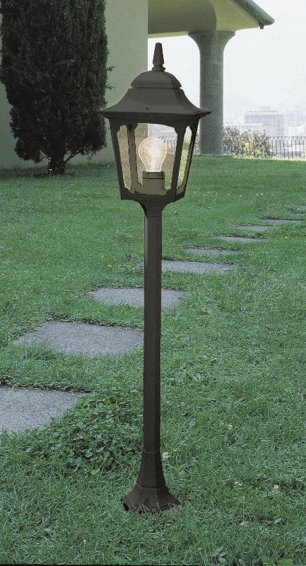 Lampa zewnętrzna stojąca Chappy 3, kolor czarny, 20,5x100 cm, z metalowym korpusem w stylu latarni. Produkt stoi na trawniku, na tle ścieżki kamiennej. Przez przezroczystą osłonę widoczna żarówka, a konstrukcja posiada dekoracyjne detale.