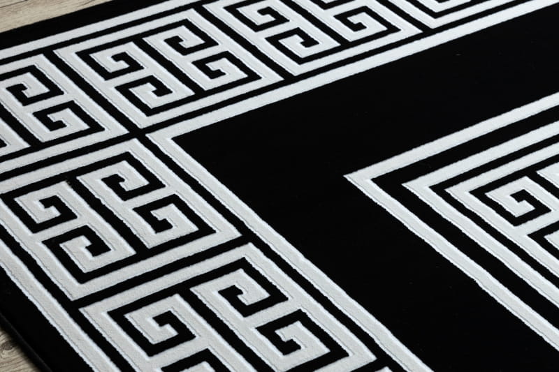 Dywan Gloria w kolorze czerni i bieli, z geometrycznym wzorem w formie greckich meanderów. Widok z boku, ukazujący detale wzoru i wykończenia. Produkt dostępny w różnych rozmiarach.