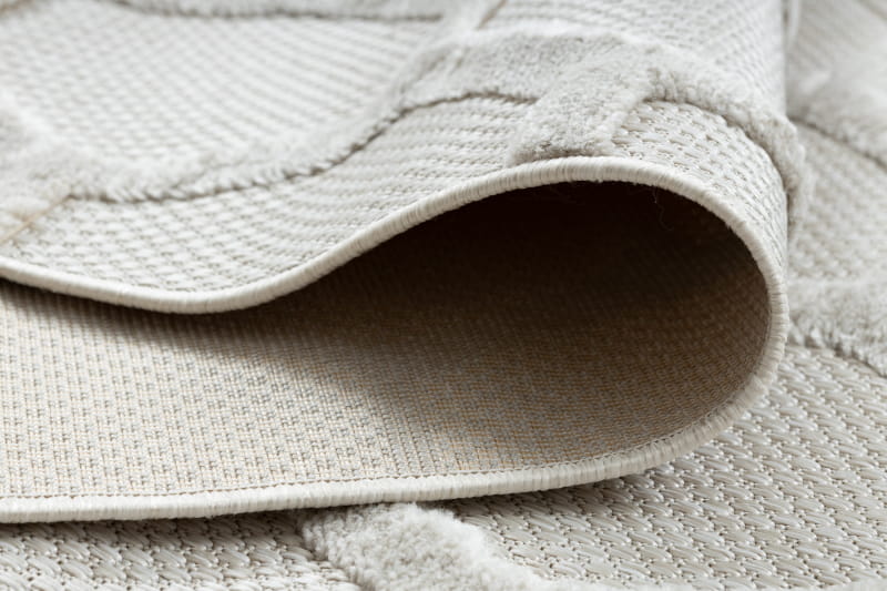 Dywan Santi w kolorze beżowym, wykonany z materiału sznurkowego o strukturze plasterka miodu. Widoczny jest brzeg dywanu oraz jego delikatna tekstura. Produkt leży na płaskiej powierzchni, z lekko podwiniętym rogiem.