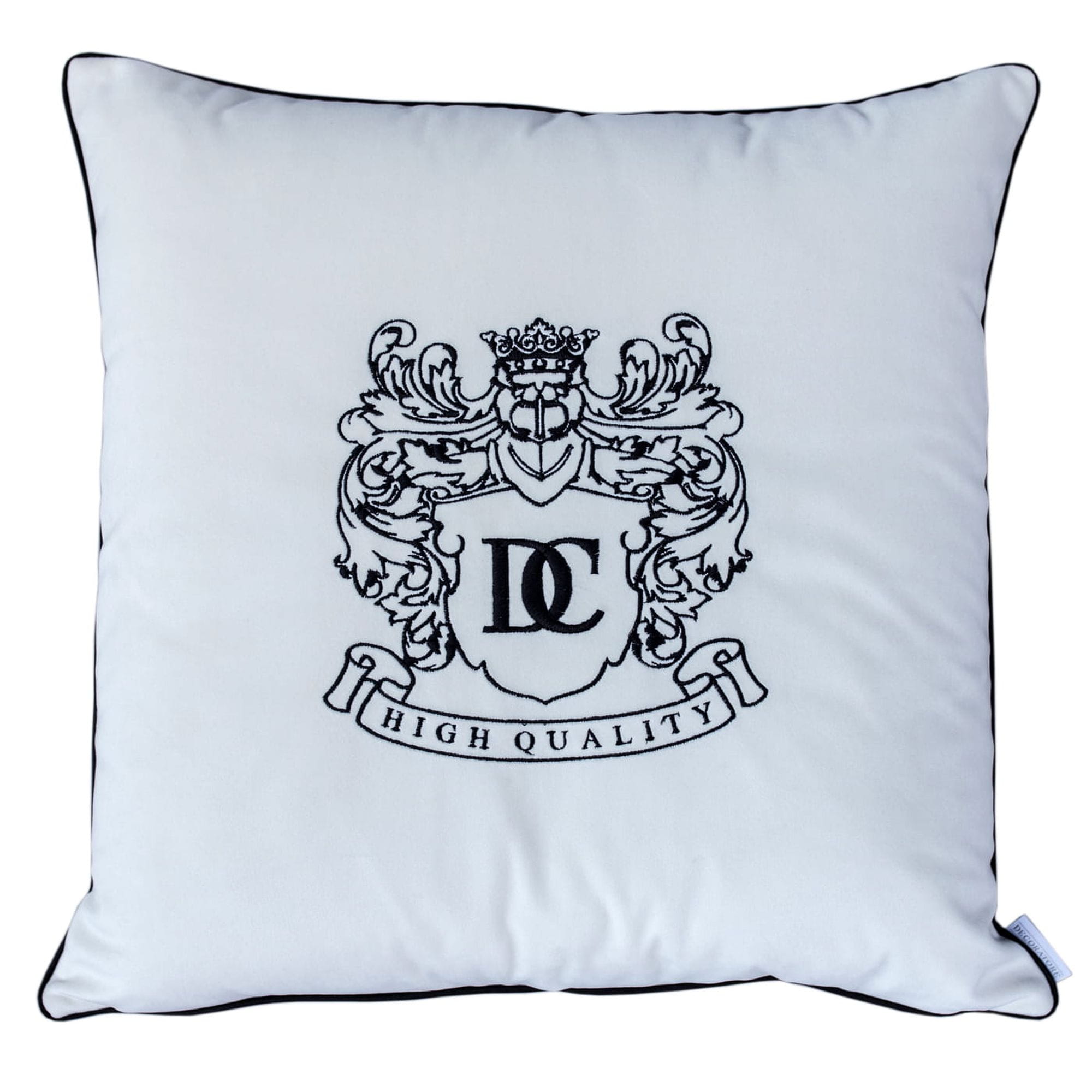 Poduszka dekoracyjna haftowana w kolorze białym z czarnym wzorem logo DC oraz napisem HIGH QUALITY. Produkt ma kwadratowy kształt, obszyty czarną lamówką, leży na płaskiej powierzchni. Idealna do aranżacji wnętrz.
