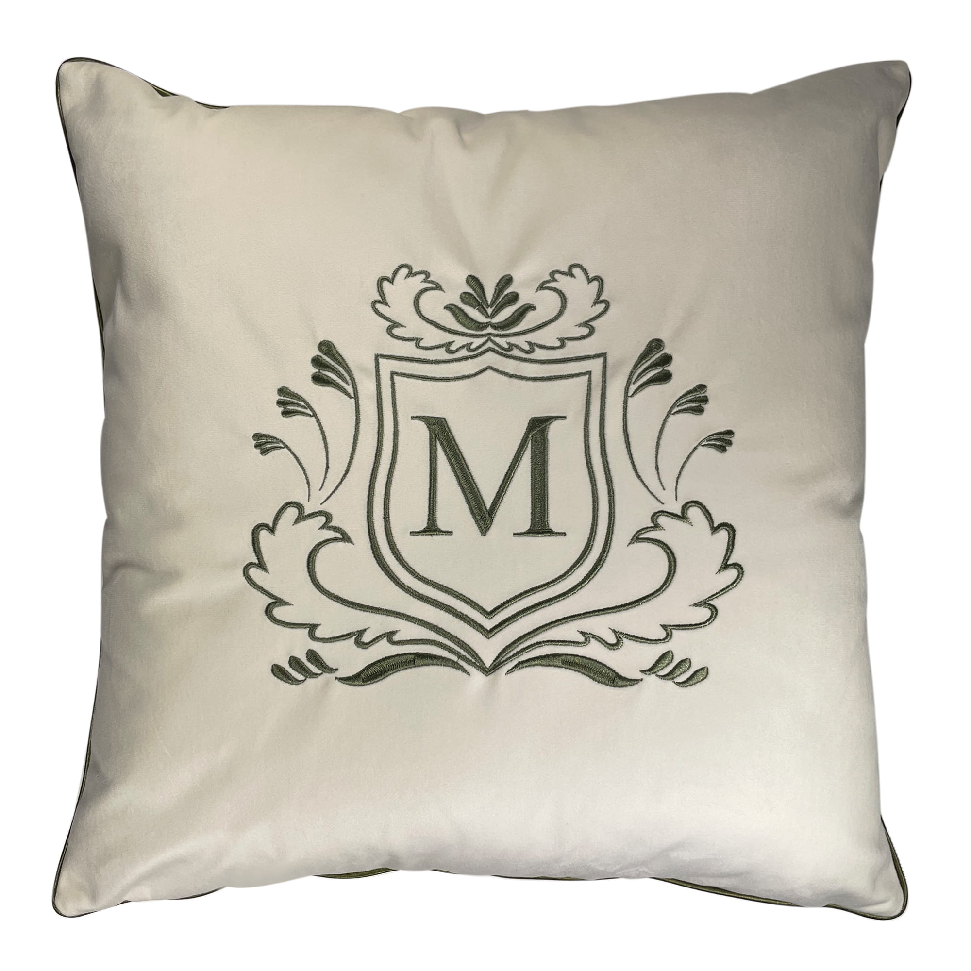 Poduszka haftowana dekoracyjna w kolorze kremowym, wykonana z welwetu. Frontalnie umieszczony monogram M w zielonym owalnym tle otoczonym ornamentalnym haftem. Produkt leży na gładkim tle, ukazując fakturę materiału oraz detale haftu.