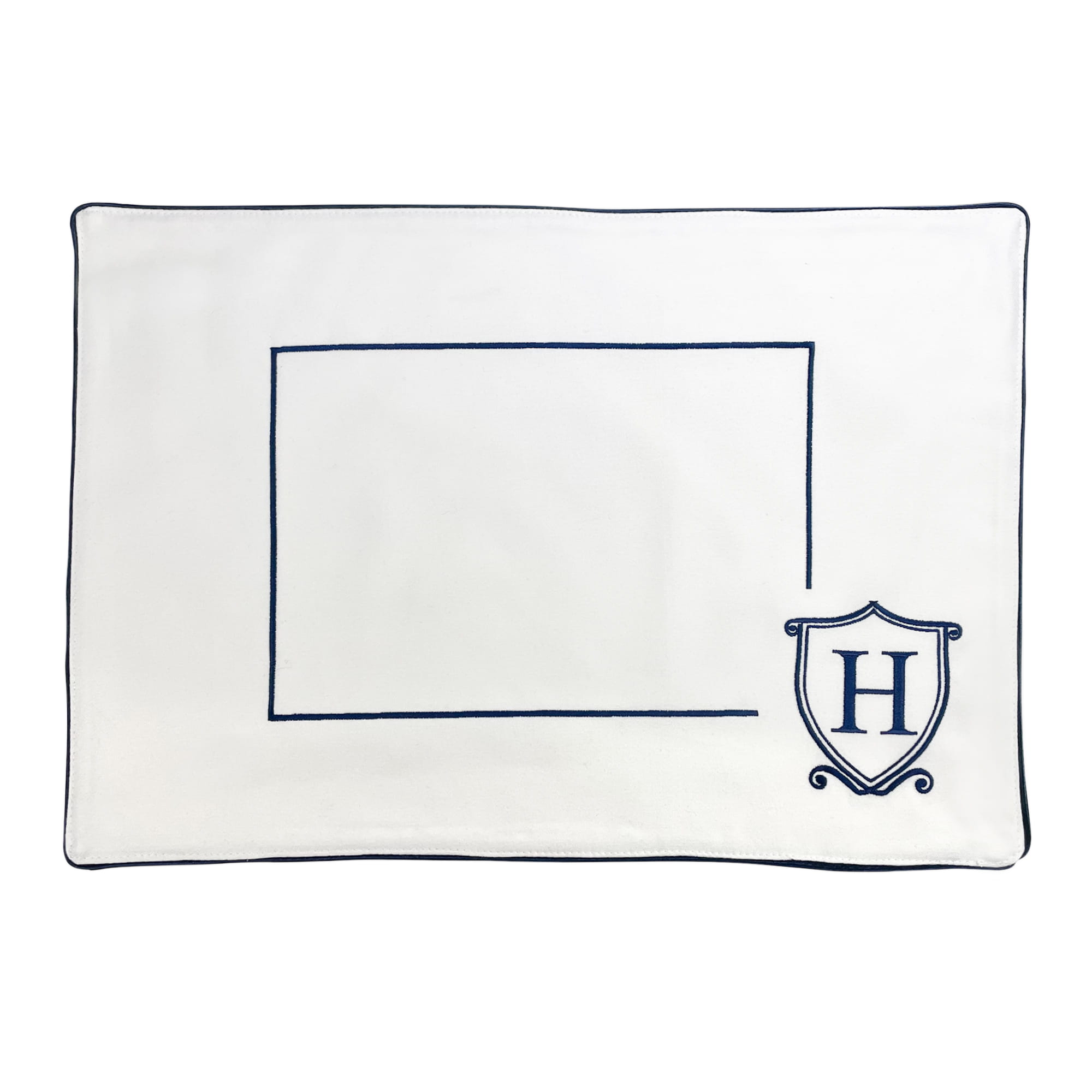 Podkładka na stół Monogram Herb w kolorze białym z granatowym wykończeniem. Z przodu widoczny kontur prostokąta na wstawienie tekstu oraz logo „H” w tarczy. Produkt leży płasko na białym tle.