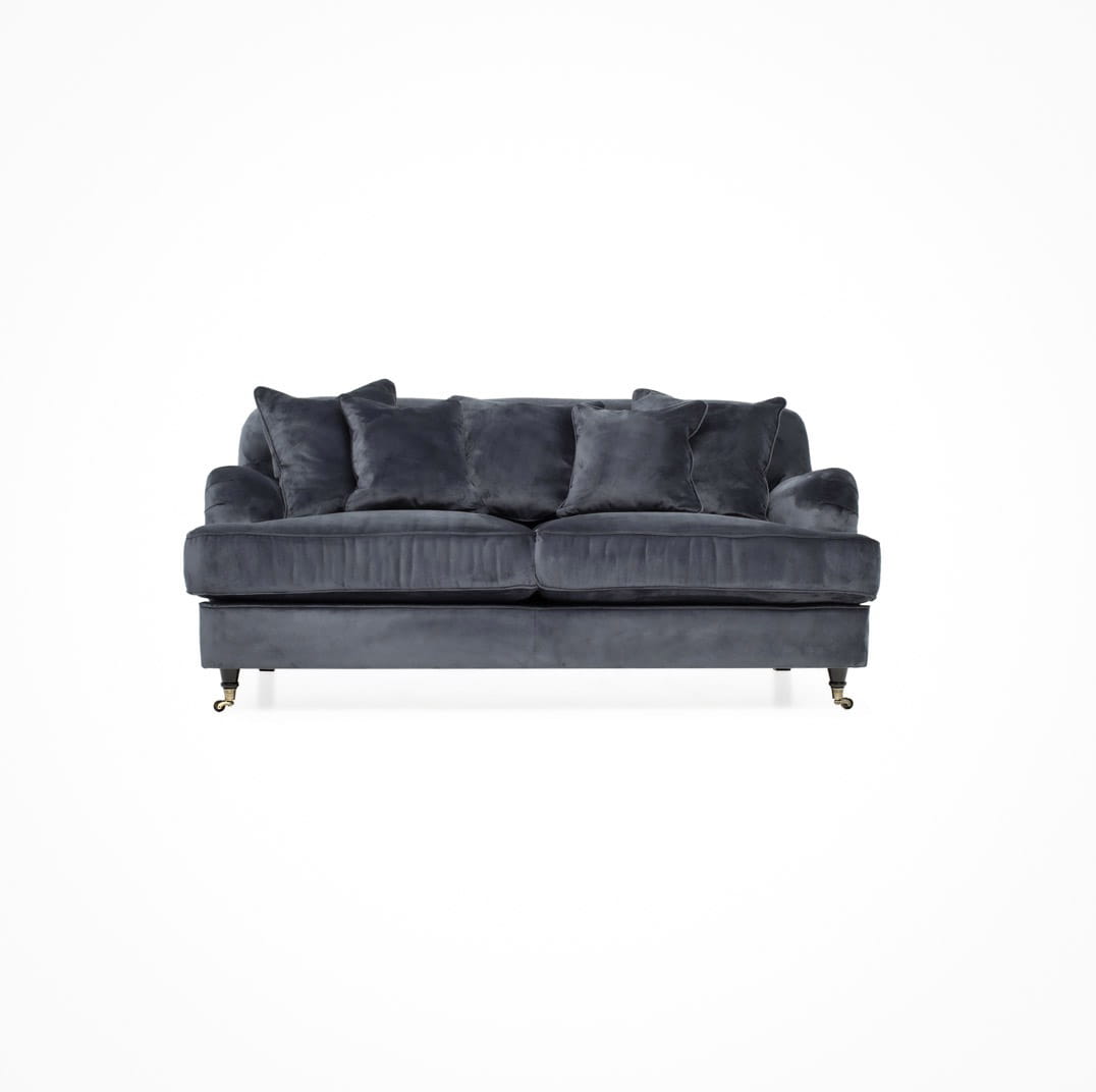 2,5 osobowa sofa Brighton w kolorze ciemnoszarym, z miękkim materiałem i poduchami. Ujęcie frontalne, produkt rozłożony na nóżkach, widoczne dwie poduszki dekoracyjne. Prosta aranżacja na białym tle. Wymiary: 180x102x84cm.