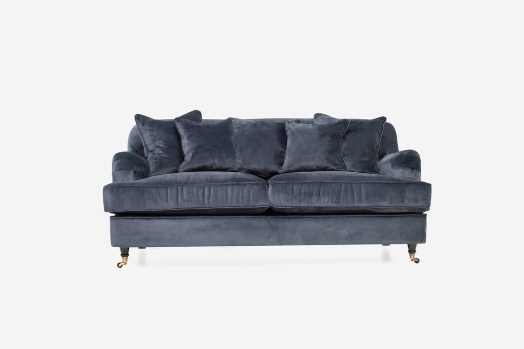 Sofa 2,5 osobowa w kolorze ciemnoszarym z miękkim, aksamitnym obiciem. Z przodu widoczne poduszki o różnych rozmiarach. Ujęcie frontalne, produkt stoi na złotych nóżkach. Wymiary: 180x102x84cm. Tekstura materiały widoczna w zbliżeniu.