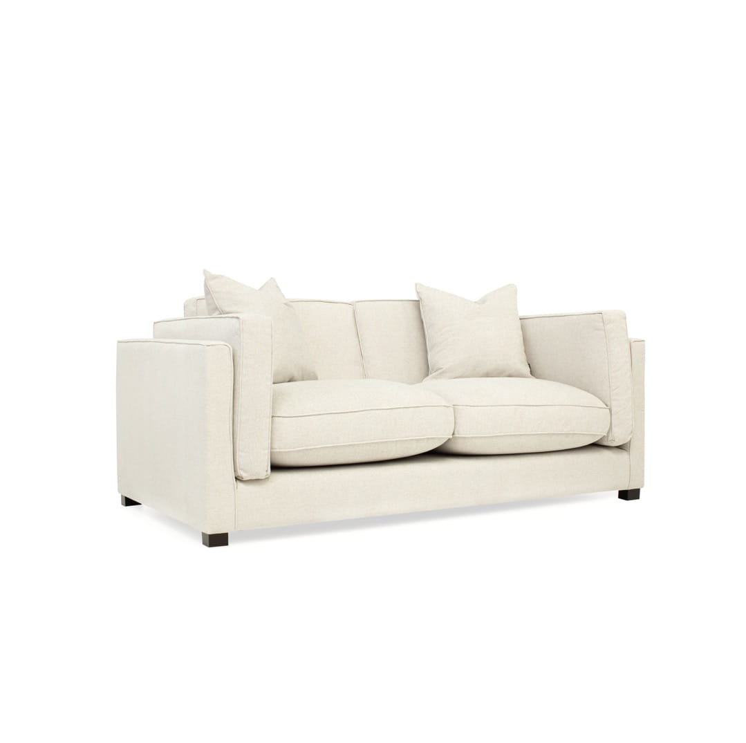 Trzyosobowa sofa Empirio w jasnym kolorze, z prostokątnymi podłokietnikami i dużymi poduszkami siedziskowymi. Ujęcie frontalne, sofa o wymiarach 215x105x78 cm, z dwoma mniejszymi poduszkami dekoracyjnymi. Produkt na białym tle.