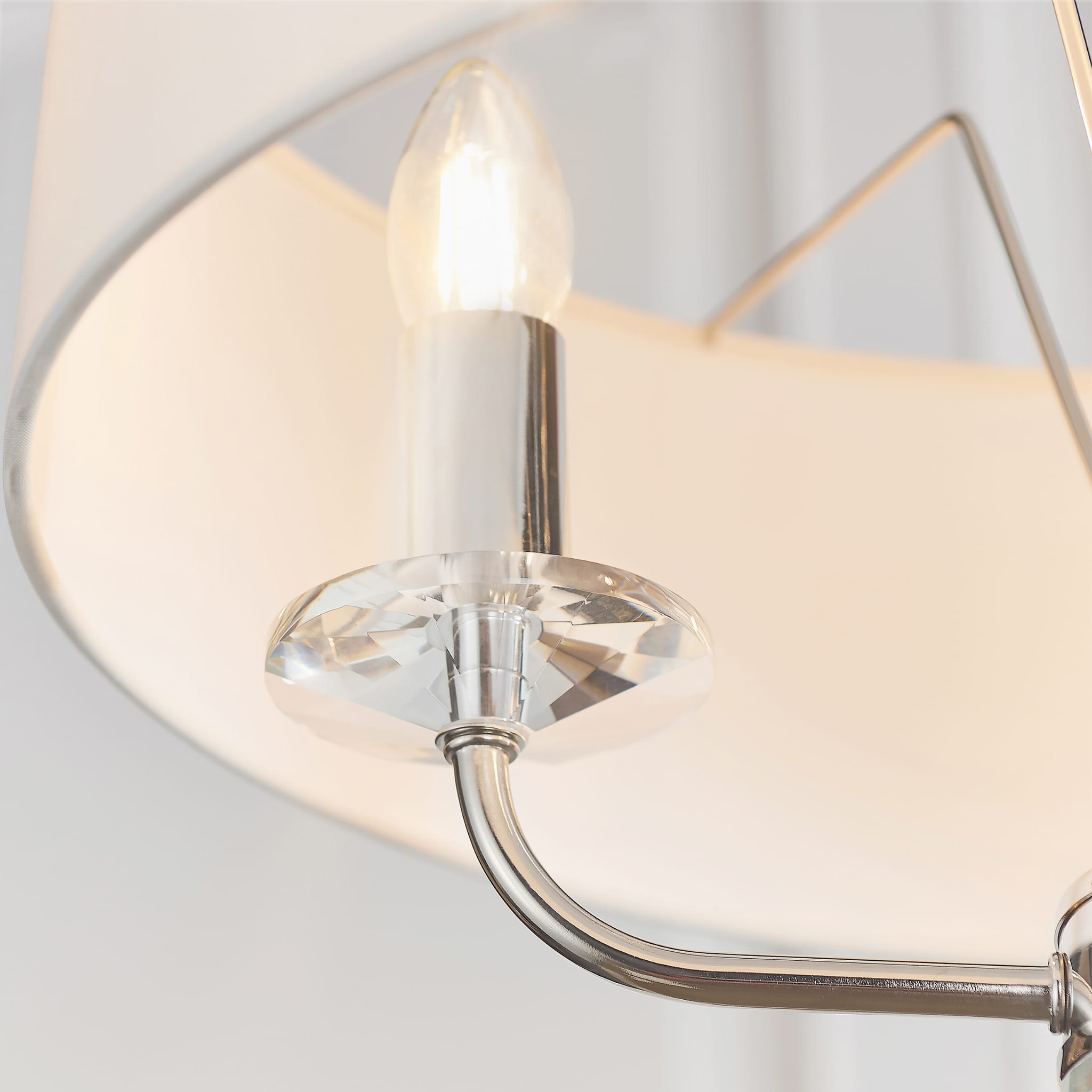 Lampa sufitowa wisząca Nixon w kolorze niklu z białym kloszem, w zbliżeniu na detal mocowania. Widoczny metalowy stelaż oraz kryształowy element, w który osadzona jest żarówka. Produkt zawieszony, idealny do nowoczesnych wnętrz.