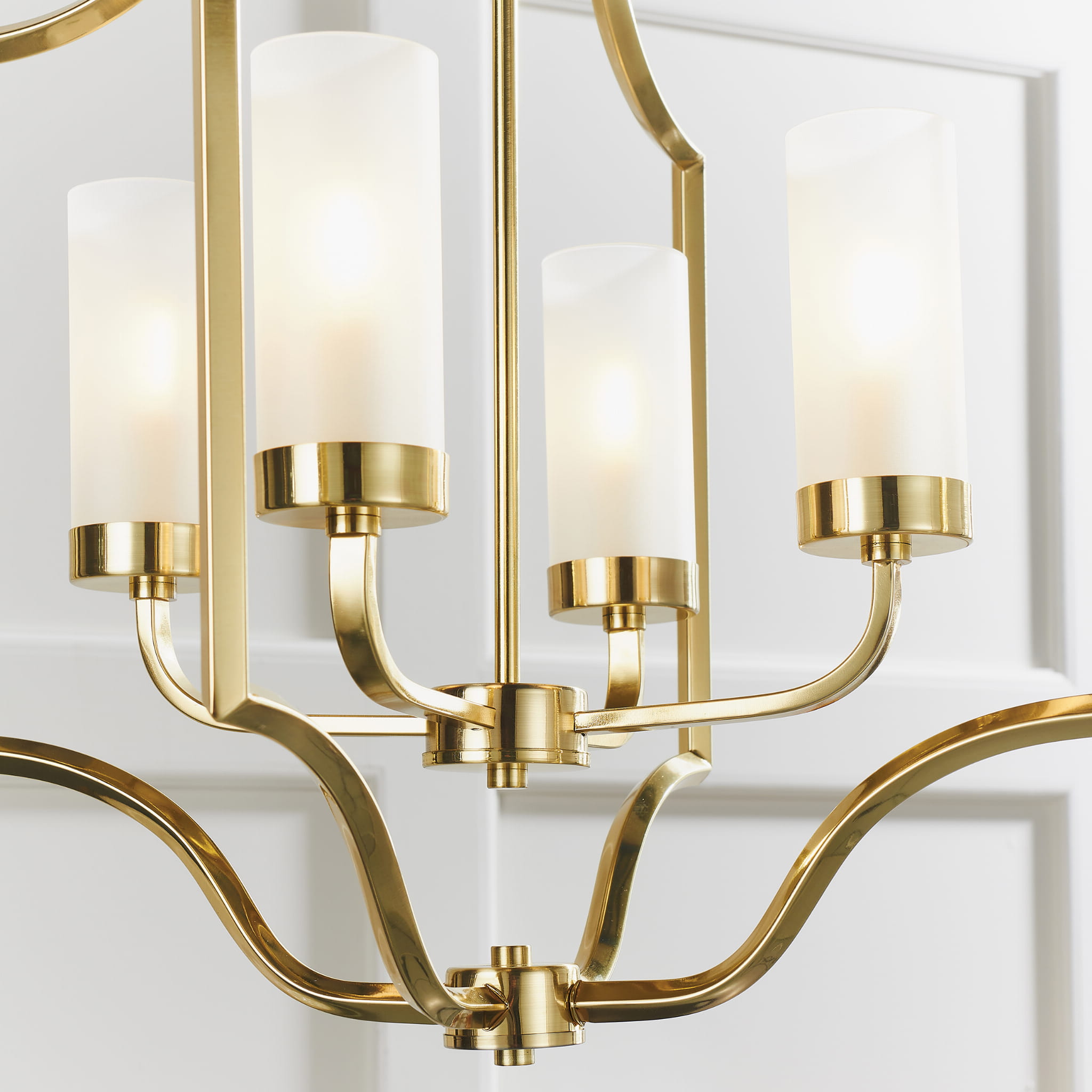 Lampa sufitowa wisząca Edrea w kolorze złotym z czterema białymi osłonami z matowego szkła. Produkt widoczny frontalnie, zawieszony, z płynnie uformowanymi ramionami. Elegancki design z nowoczesnymi akcentami. Tło proste, jasne.