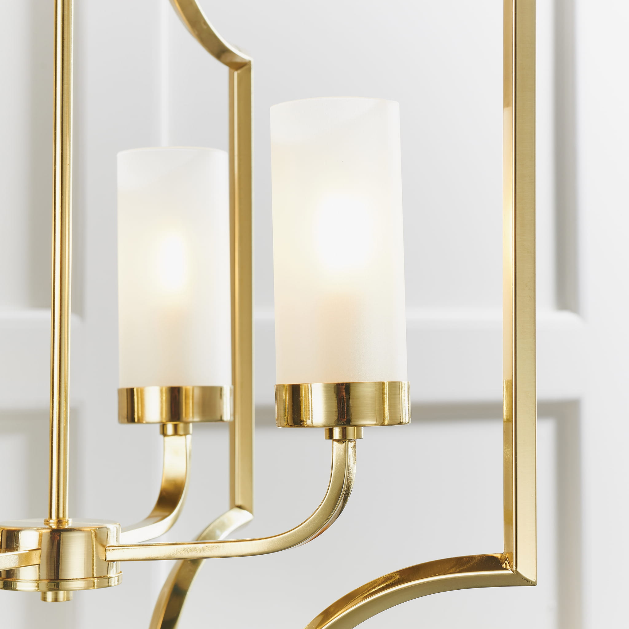 Lampa sufitowa wisząca Edrea z metalowym stelażem w złotym kolorze i matowym, białym kloszem. Zbliżenie na dwa klosze, każdy z pierścieniem dekoracyjnym. Produkt prezentowany w jasnym wnętrzu z białym tłem. Długość 100 cm.