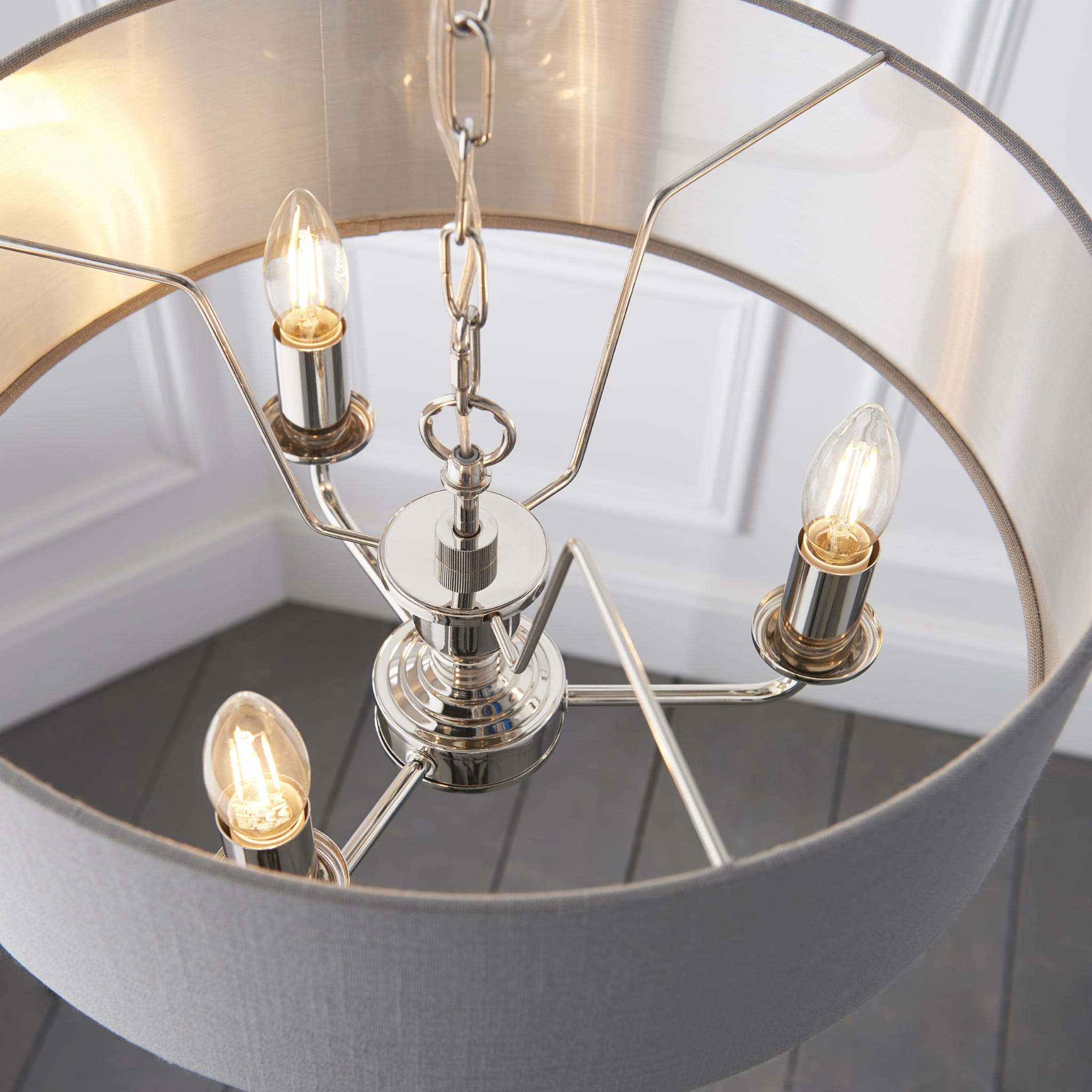 Lampa sufitowa wisząca Highclere o średnicy 35 cm, z metalową podstawą w kolorze srebrnym i materiałowym kloszem w odcieniu szarym. Produkt widoczny z góry, w ujęciu ukazującym trzy żarówki i łańcuch. Tło białe, minimalistyczne.