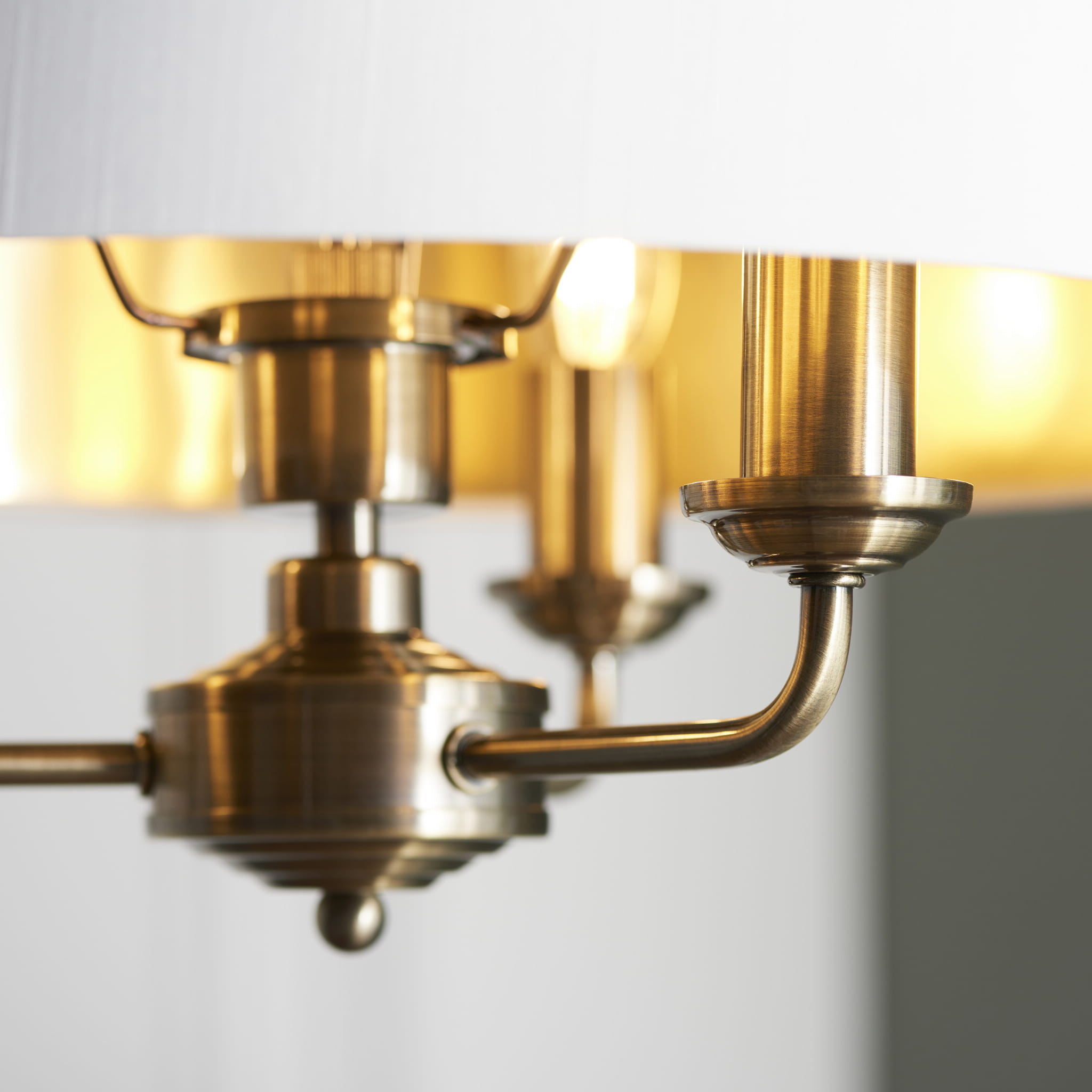 Lampa sufitowa wisząca Highclere w kolorze antycznego brązu z tkaninowym kloszem. W prezentacji w zbliżeniu widoczne metalowe elementy mocujące oraz struktura klosza. Produkt zawieszony, z szerokim rozstawem ramion.
